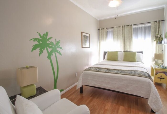 Hotel Royal gay-friendly room. Bedroom with palm tree wall art, white bedding, and chair. Comfortable gay travel lodging.