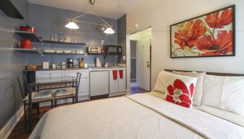 Hotel Royal gay-friendly room. Studio apartment interior with bed, kitchenette, dining table, and floral art. Gay travel lodging.