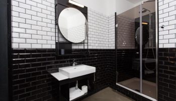 Hotel Rum Budapest gay-friendly bathroom. Black and white tiled walls, modern sink, round mirror, and glass-enclosed shower. Stylish design.