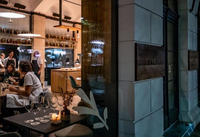 Salt restaurant at Hotel Rum Budapest, a gay-friendly hotel. Interior view with diners, wine glasses, and kitchen staff visible.