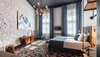Gay-friendly Hotel Rum Budapest room. Stylish interior with peacock carpet, brick wall, modern art, blue curtains, & unique lighting. Upscale design.
