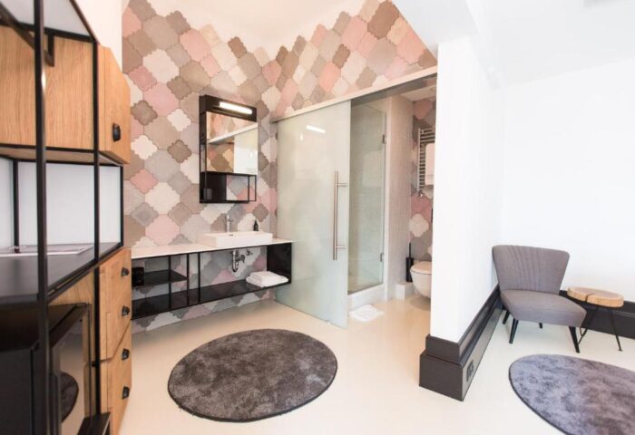 Hotel Rum Budapest gay-friendly bathroom. Modern design with patterned tiles, glass shower, sink, and chair. Stylish, comfortable stay.