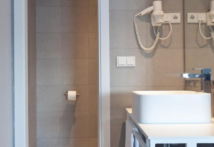 Hotel Ryans La Marina gay-friendly hotel bathroom. Modern design with white sink, gray tiles, and shower. Ideal for gay travel.