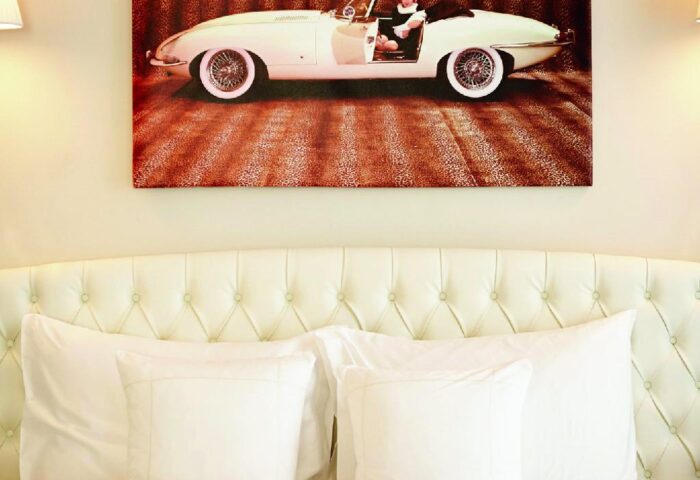 Hotel Sans Souci Wien bedroom. Queen bed with white linens, tufted headboard. Above the bed hangs a vintage car photo. Gay-friendly hotel.