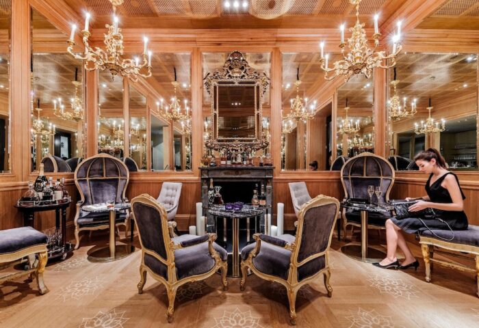 Hotel Sans Souci Wien's gay-friendly lounge. Ornate chairs, a fireplace, and chandeliers create a luxurious, inviting space. Woman sitting.