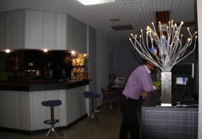 Hotel Santa Faz, adults only, gay-friendly hotel. Lobby bar area with stools, snacks, and a person at the front desk. Modern design.