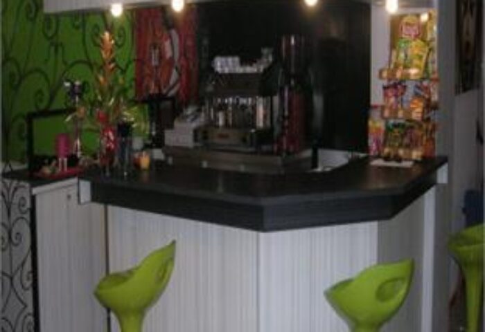 Hotel Santa Faz adults-only gay-friendly hotel bar. Green bar stools, espresso machine, and snacks. A welcoming space for gay travelers.