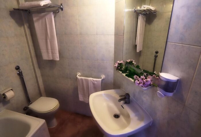 Bathroom at Hotel Santa Faz, an adults-only, gay-friendly hotel. Features a sink, toilet, bathtub, mirror, and fresh flowers.