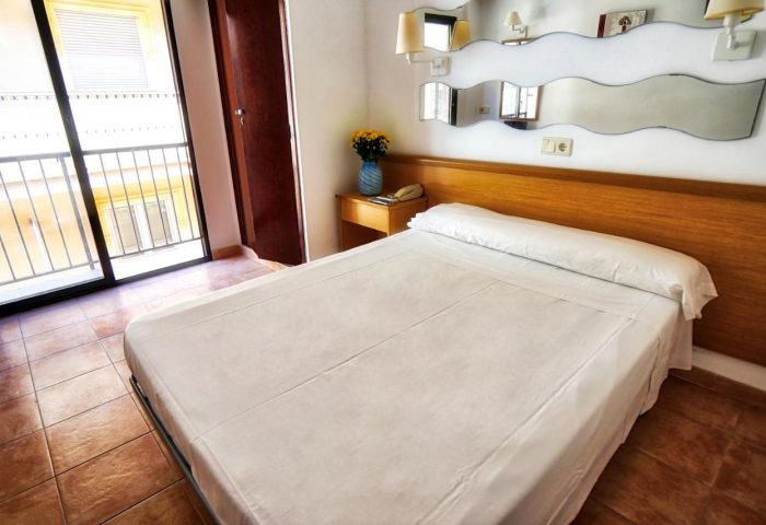 Hotel Santa Faz, a gay-friendly adults-only hotel. Bedroom with double bed, balcony, and unique mirror feature. Ideal for gay travel.