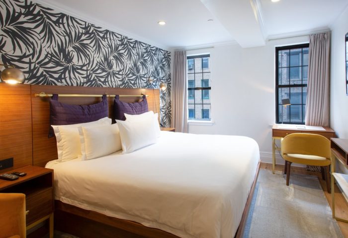 Hotel Scherman gay-friendly room. Queen bed, desk, and city views. Modern decor, purple pillows, and stylish wallpaper. Comfortable stay.