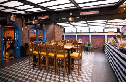 Hotel Scherman's gay-friendly dining area. Wooden chairs with yellow cushions surround tables. Brick walls, unique floor pattern, and bright decor.