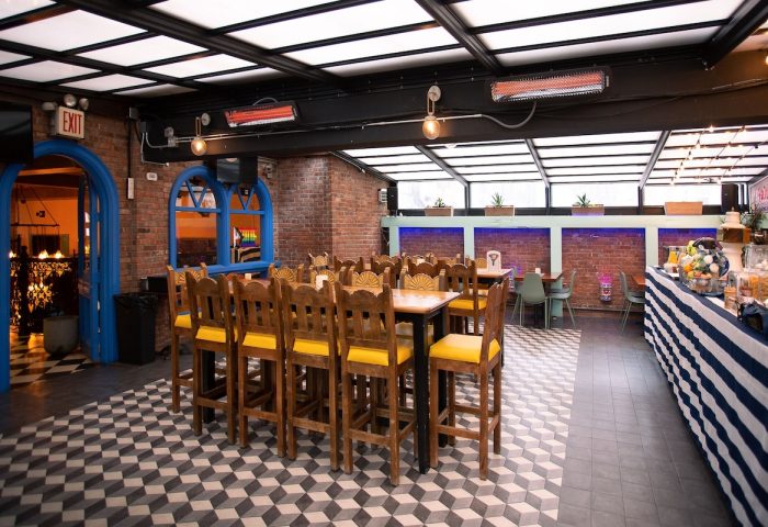 Hotel Scherman's gay-friendly dining area. Wooden chairs with yellow cushions surround tables. Brick walls, unique floor pattern, and bright decor.