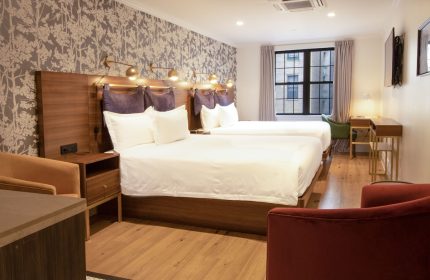 Hotel Scherman gay-friendly room. Two beds with white linens, wood headboards, stylish wallpaper, and cozy seating for a relaxing stay.