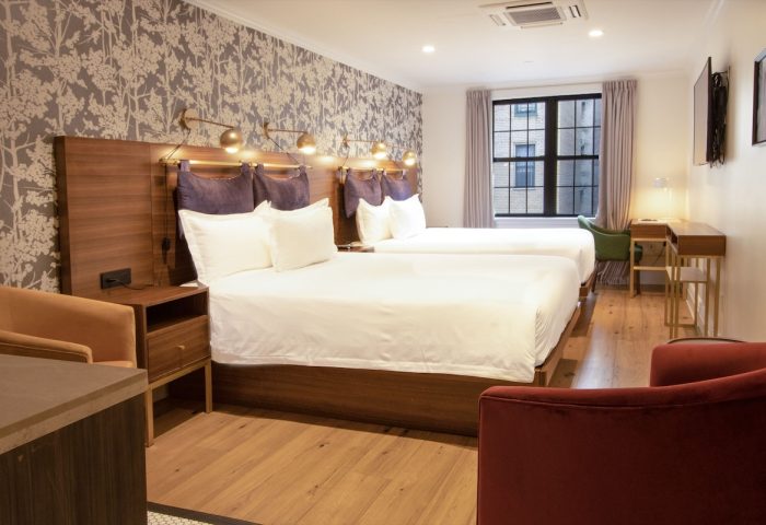 Hotel Scherman gay-friendly room. Two beds with white linens, wood headboards, stylish wallpaper, and cozy seating for a relaxing stay.