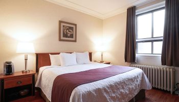 Hotel St-Denis bedroom. Gay-friendly hotel room featuring a queen bed, nightstands, lamps, and a window with brown curtains.