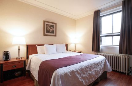 Hotel St-Denis bedroom. Gay-friendly hotel room featuring a queen bed, nightstands, lamps, and a window with brown curtains.