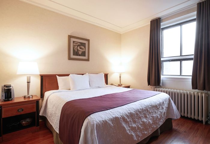 Hotel St-Denis bedroom. Gay-friendly hotel room featuring a queen bed, nightstands, lamps, and a window with brown curtains.