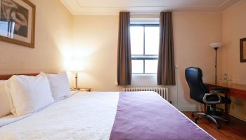 Hotel St-Denis bedroom. Gay-friendly hotel room featuring a bed with white linens and a desk with a black office chair. Gay travel advice.
