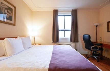 Hotel St-Denis bedroom. Gay-friendly hotel room featuring a bed with white linens and a desk with a black office chair. Gay travel advice.