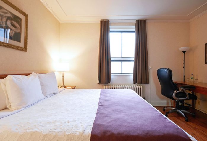 Hotel St-Denis bedroom. Gay-friendly hotel room featuring a bed with white linens and a desk with a black office chair. Gay travel advice.