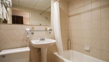 Bathroom at Hotel St-Denis, a gay-friendly hotel. Features a white sink, toilet, bathtub with shower curtain, and tiled walls.