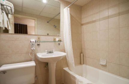 Bathroom at Hotel St-Denis, a gay-friendly hotel. Features a white sink, toilet, bathtub with shower curtain, and tiled walls.