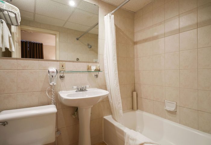 Bathroom at Hotel St-Denis, a gay-friendly hotel. Features a white sink, toilet, bathtub with shower curtain, and tiled walls.