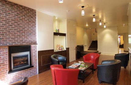 Hotel St-Denis's gay-friendly lounge area. Red and black armchairs surround a coffee table with magazines. A fireplace adds warmth.