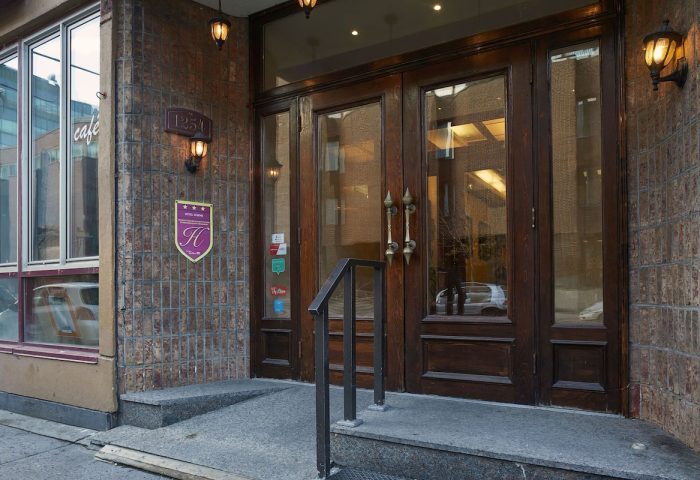 Hotel St-Denis entrance, a gay-friendly hotel. The facade features a brick wall, wooden doors, and a sign with the hotel's logo.