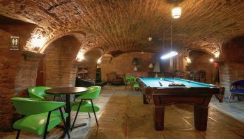 Hotel St-Denis' gay-friendly interior. Stone-walled game room with pool table, green chairs, and arched ceiling. Gay travel lodging.