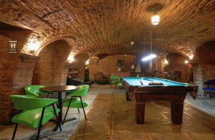Hotel St-Denis' gay-friendly interior. Stone-walled game room with pool table, green chairs, and arched ceiling. Gay travel lodging.