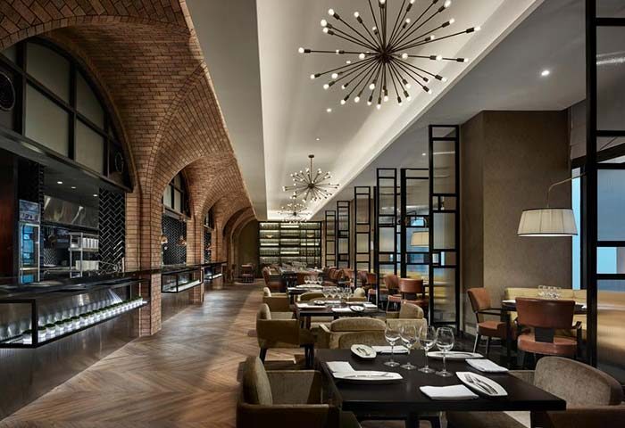 Gay-friendly Hotel Stripes Kuala Lumpur, Autograph Collection restaurant. Brick arches, modern lighting, and set tables.