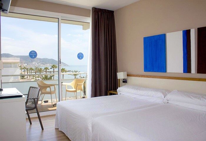 Hotel Subur Maritim gay-friendly room. Pet-friendly hotel with sea view balcony. Room with two beds, desk, and modern art. Gay travel.