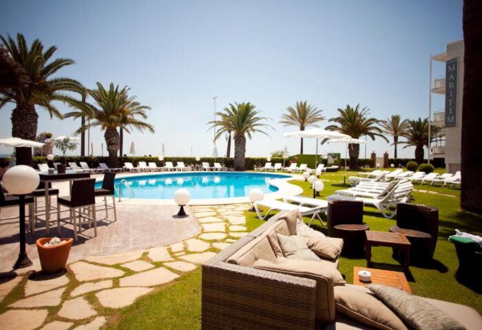 Hotel Subur Maritim's pool area. This gay-friendly, pet-friendly hotel offers a relaxing space with palm trees, sunbeds, and lounge seating.