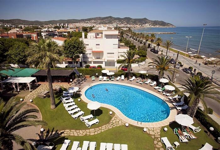 Hotel Subur Maritim pool view. Gay-friendly, pet-friendly hotel in Sitges near the beach. Palm trees, lounge chairs, sunny day.