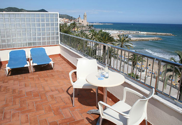 Hotel Subur Sitges balcony view. Gay-friendly, pet-friendly hotel with beach views. Table, chairs, and loungers offer a relaxing space.