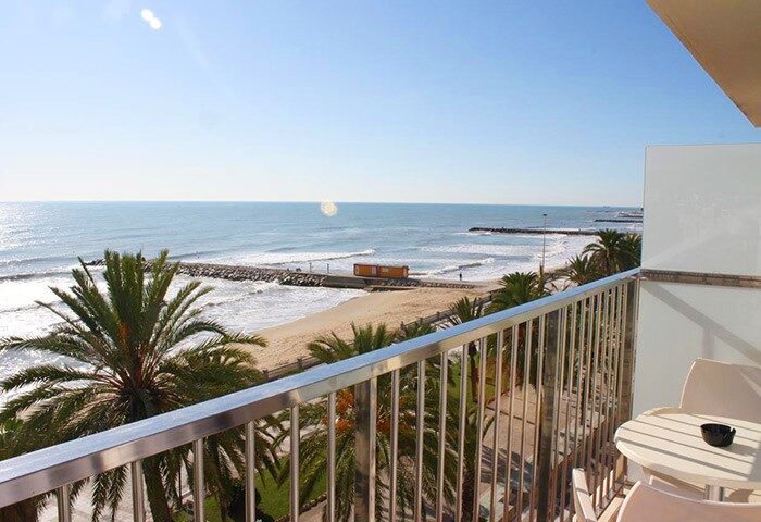 Balcony view at Hotel Subur Sitges, a gay-friendly, pet-friendly hotel. Palm trees, beach, and ocean visible. Perfect for gay travel.