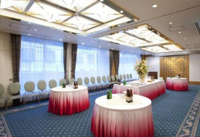 Hotel Sunlite Shinjuku's event space. The gay-friendly hotel features tables with red-ombre cloths, chairs, and a blue patterned carpet.