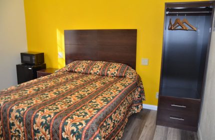 Hotel Sunrise gay-friendly room. Queen bed with colorful patterned bedding, yellow wall, microwave, mini-fridge, and closet.