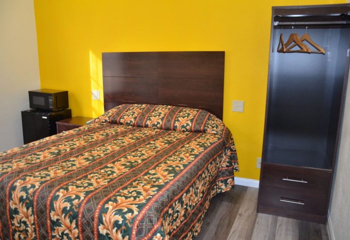 Hotel Sunrise gay-friendly room. Queen bed with colorful patterned bedding, yellow wall, microwave, mini-fridge, and closet.