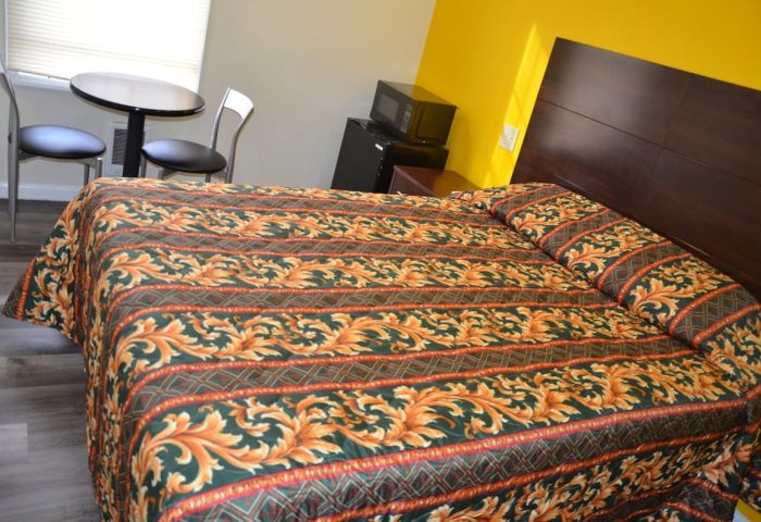 Hotel Sunrise gay-friendly room. Features a bed with patterned bedding, a small table with chairs, microwave, and mini-fridge.
