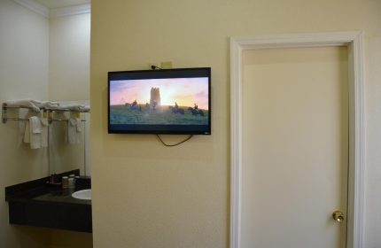 Hotel Sunrise gay-friendly room: TV showing riders on horseback, next to a door and bathroom sink. Ideal for gay men travel advice.