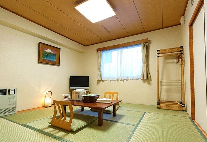 Hotel Tateshina, a gay-friendly hotel. Traditional Japanese room with tatami mats, low table, seating cushions, and a window. Relaxing space.