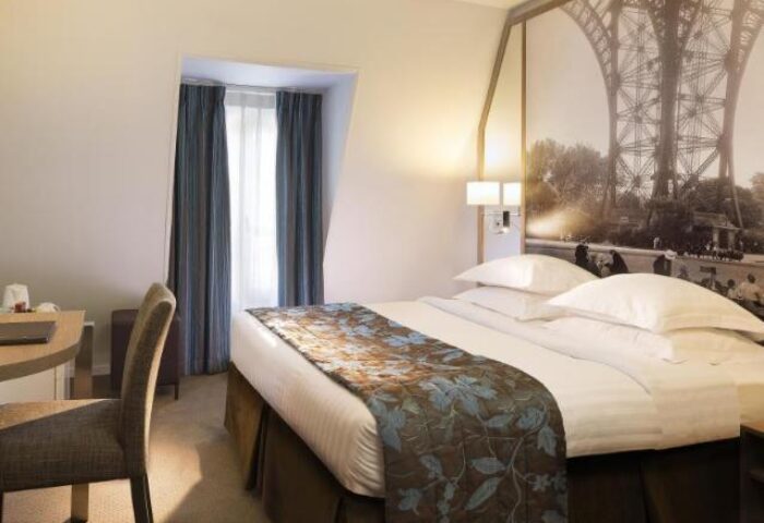 Hotel Turenne Le Marais room. Gay-friendly, pet-friendly hotel bedroom with Eiffel Tower mural. Desk, chair, bed with floral throw. Paris lodging.