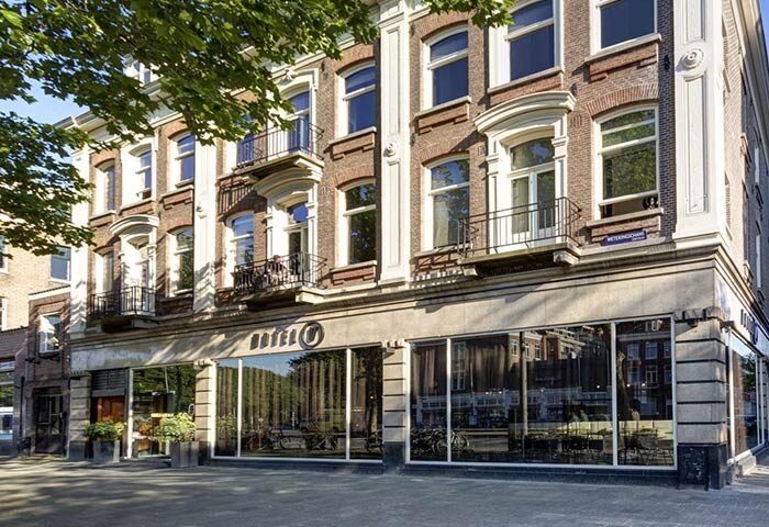 Hotel V Frederiksplein, a gay-friendly hotel in Amsterdam. Exterior view of the hotel with its brick facade and large windows.