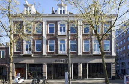 Hotel V Frederiksplein, a gay-friendly hotel in Amsterdam. The building's facade features brickwork, large windows, and a modern design.