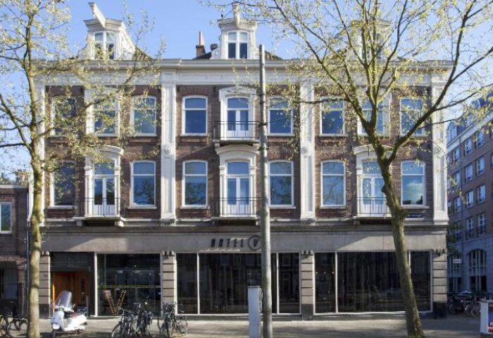 Hotel V Frederiksplein, a gay-friendly hotel in Amsterdam. The building's facade features brickwork, large windows, and a modern design.