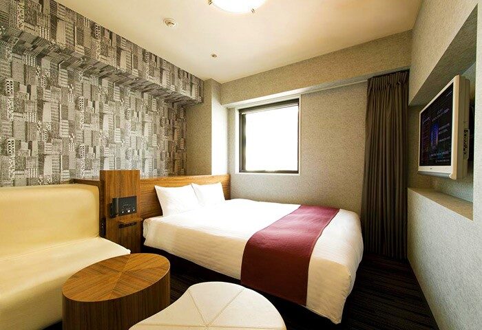 Hotel Villa Fontaine Tokyo-Shinjuku room. Gay-friendly hotel with bed, sofa, TV, table, and city-themed wallpaper. Modern design for gay travelers.
