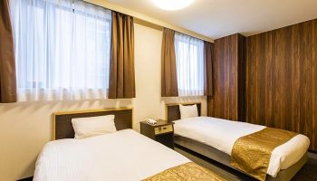 Hotel Wing International Shinjuku room. Twin beds, white linens, gold accents. Gay-friendly hotel in Shinjuku, Japan. Clean, modern design.