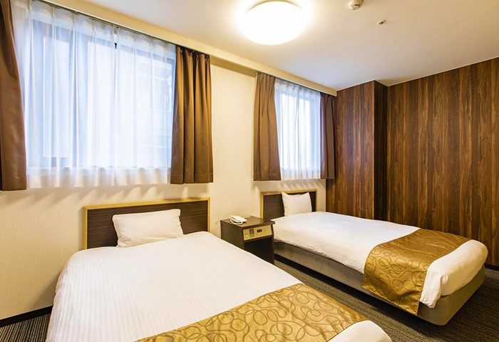 Hotel Wing International Shinjuku room. Twin beds, white linens, gold accents. Gay-friendly hotel in Shinjuku, Japan. Clean, modern design.